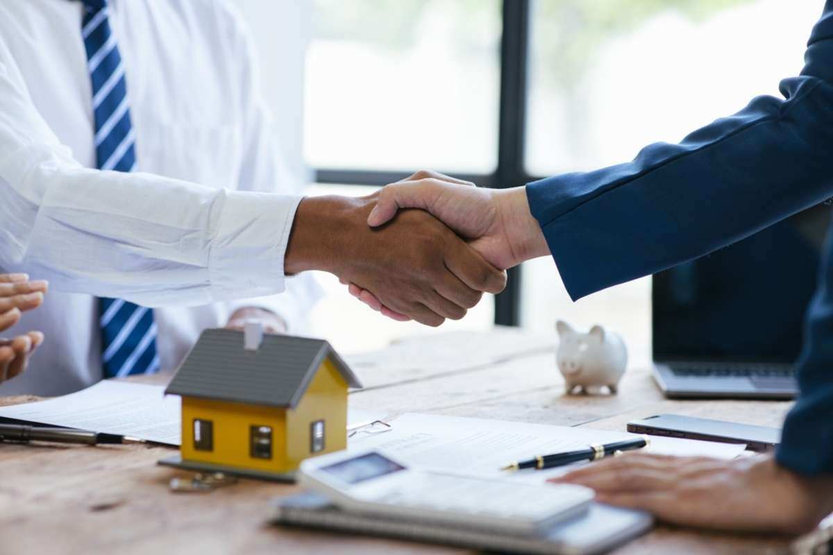 A handshake near a model house and piggy bank