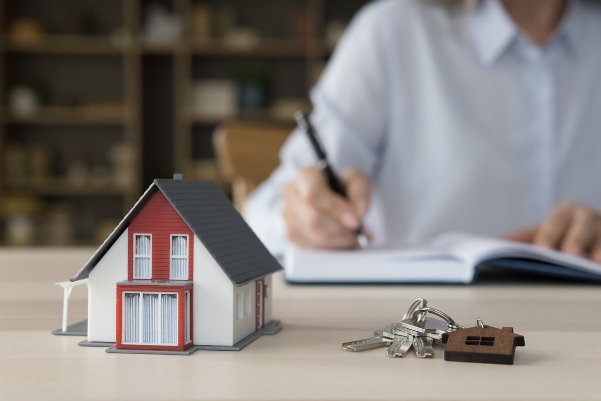 A person sat at a desk conducting a tenant screening process with a small home and keys on the table.