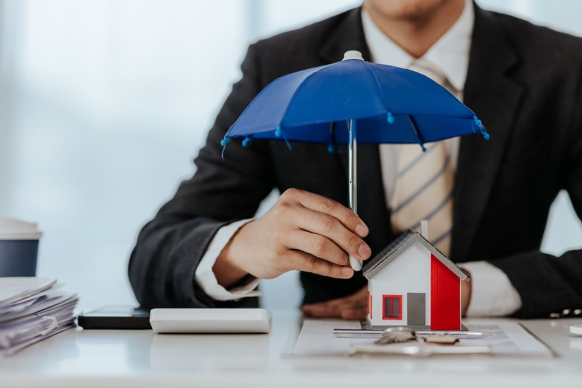 Property manager holding umbrella over house model to represent protection