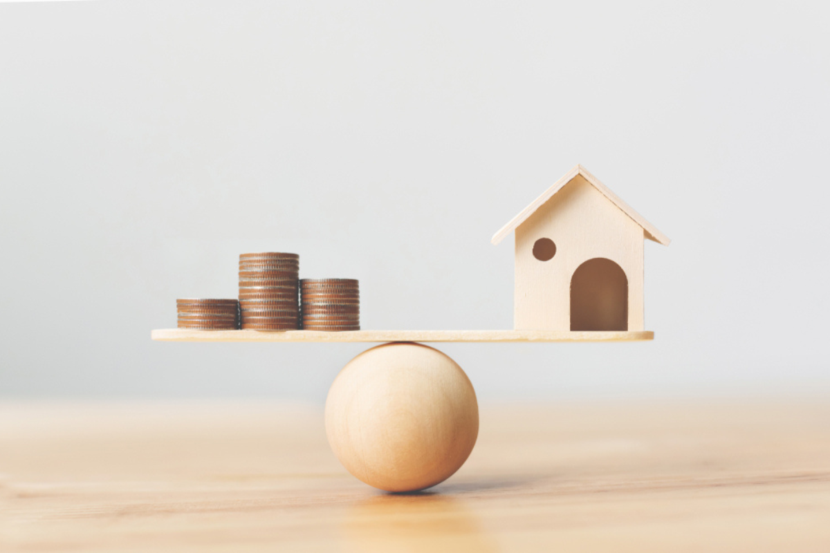 A wooden house and coins on a wooden scale