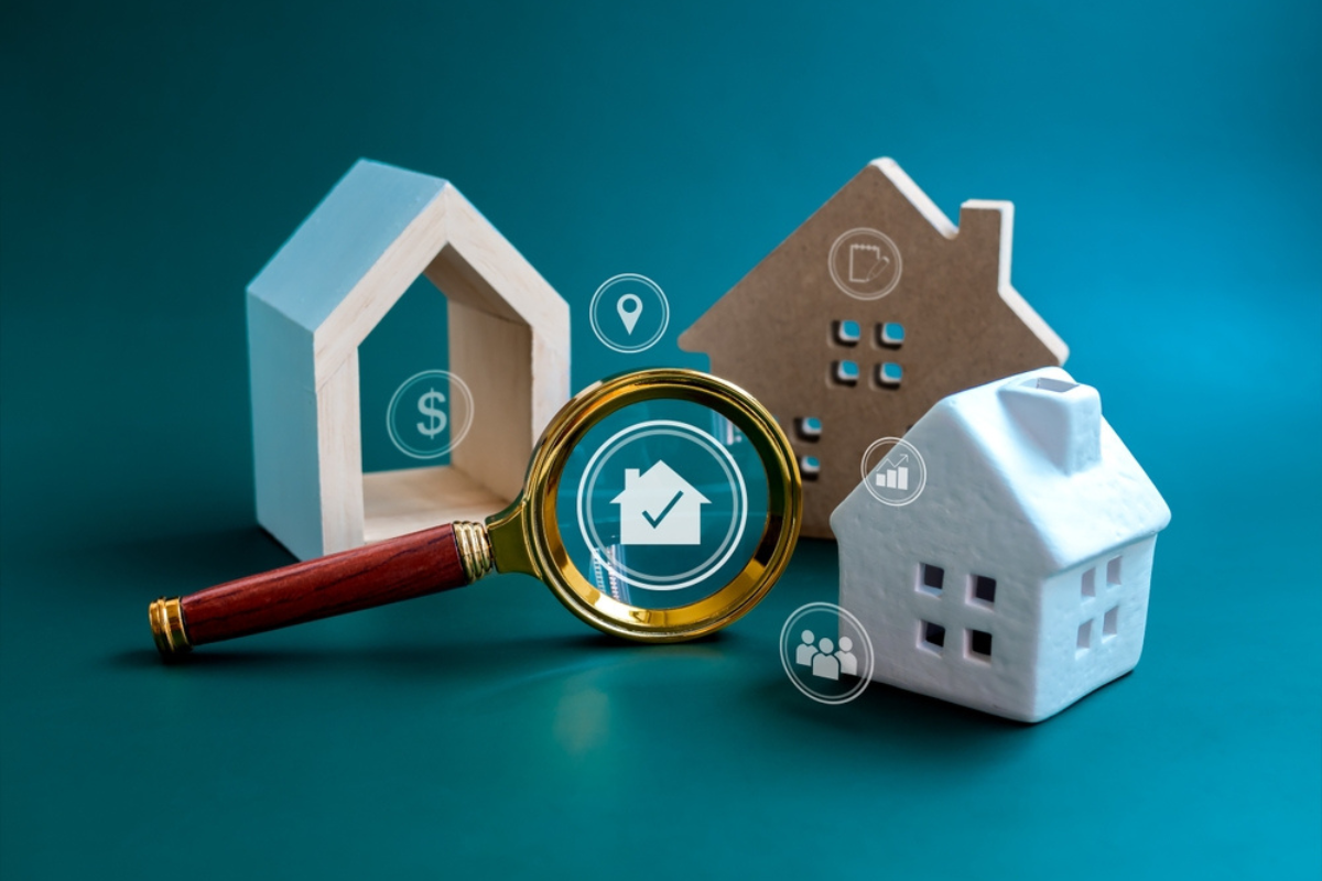 A magnifying glass with wooden house models and real estate symbols.