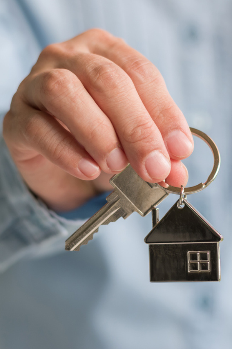 A man holding keys with a house keychain.